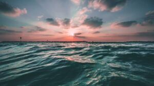 a view of an ocean with light waves in the foreground and a sunset in the background