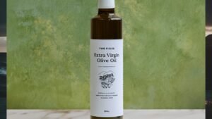 A bottle of Two Fields Olive oil stands against a blurred green background